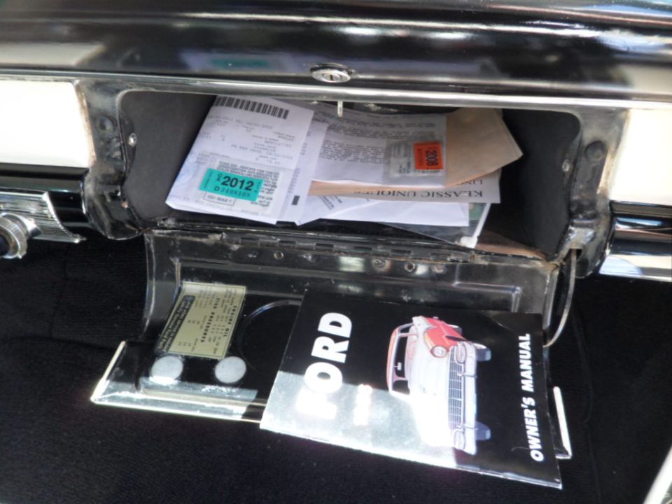 Glove compartment open, showing papers and a 1956 Ford owner's manual