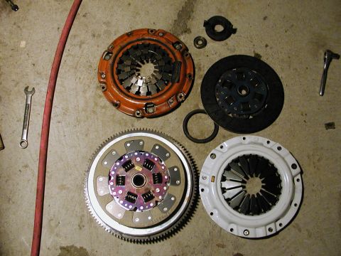 1996 Ford Probe - Various clutch components, including a pressure plate, clutch disc, and flywheel, are displayed on a concrete surface alongside tools.