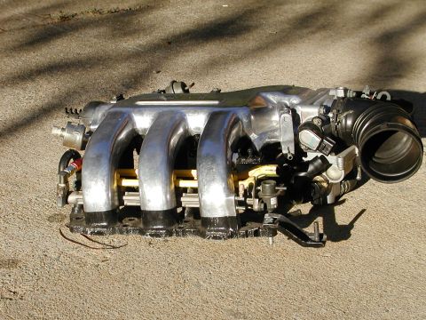 1996 Ford Probe - Engine intake manifold with four runners and throttle body, resting on pavement.
