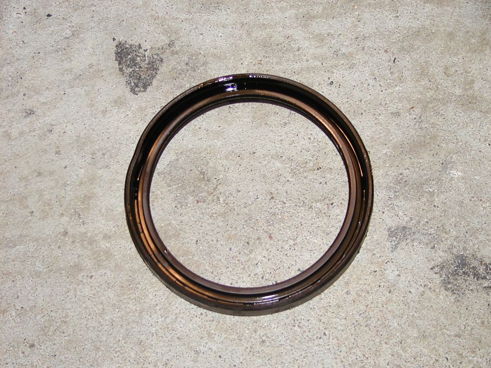 Oil seal on concrete floor. The seal is dark brown and metallic with visible wear