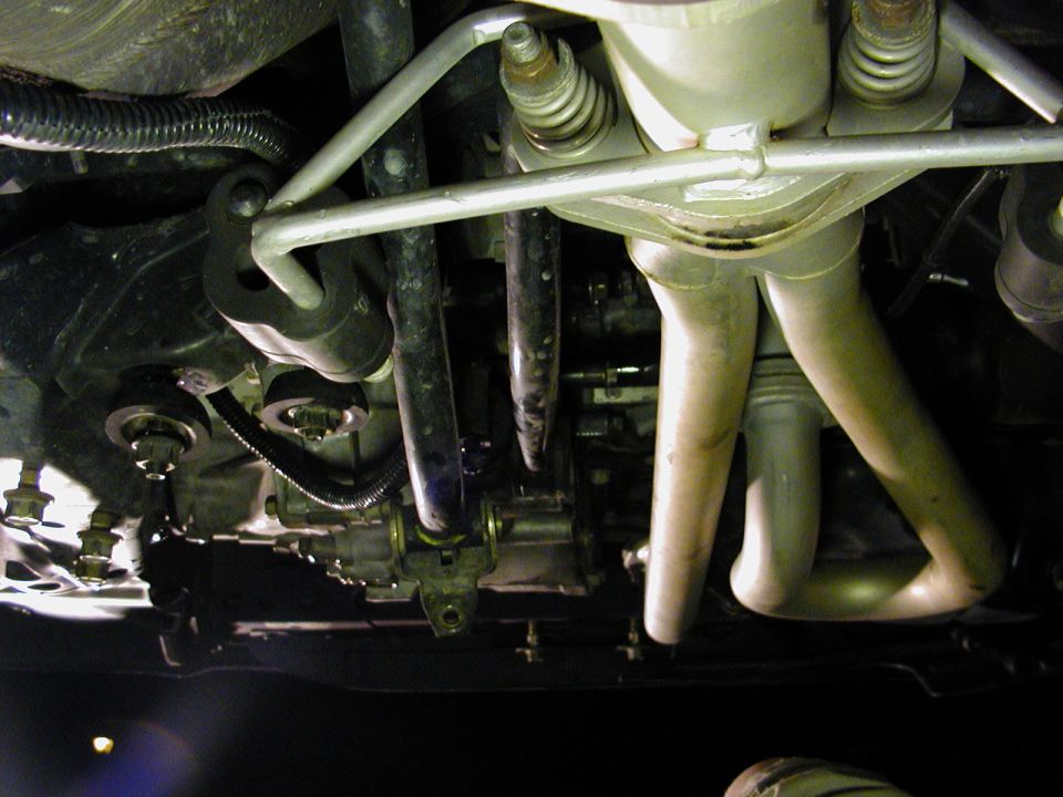 Underside view of vehicle suspension and exhaust pipes, showing metal components and rubber bushings