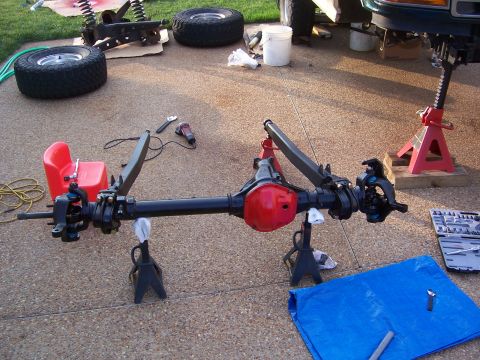 1992 Ford Bronco - A front axle assembly, likely from an SUV or truck, is supported by jack stands on a paved surface, with tools and tires nearby.