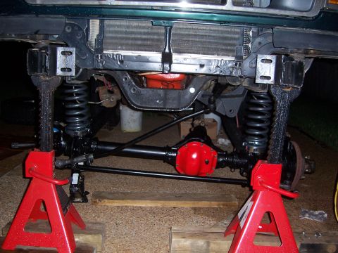 1992 Ford Bronco - Front axle and suspension components are visible, supported by red jack stands, with a bright red differential housing.