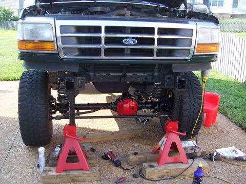 1992 Ford Bronco - The front end of a Ford truck is elevated on jack stands, revealing its suspension and drivetrain components.