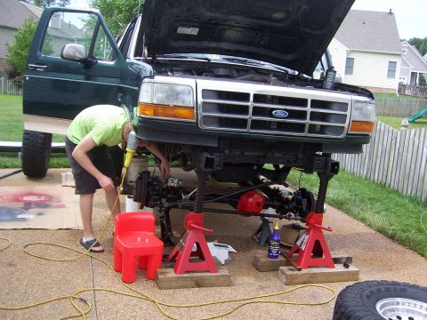1992 Ford Bronco - A green 1992 Ford Bronco is raised on jack stands as a person works on the front suspension and drivetrain.