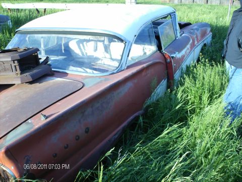 1958 Ford Fairlane - Rusty 1958 Ford Fairlane sits abandoned in tall grass, driver's door open.