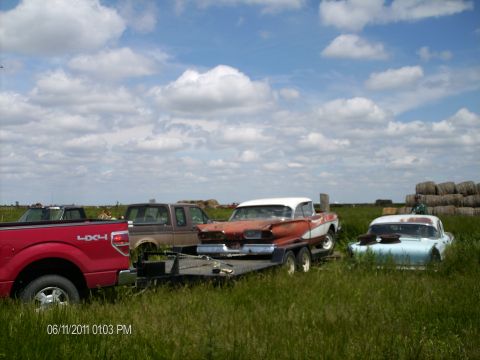 1958 Ford Fairlane - Several vehicles, including a 1958 Ford Fairlane, are parked in a grassy field under a cloudy sky.