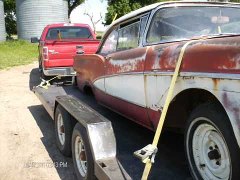 1958 Ford Fairlane - A red Ford pickup tows a weathered 1957 Ford on a trailer, showing signs of rust and wear.