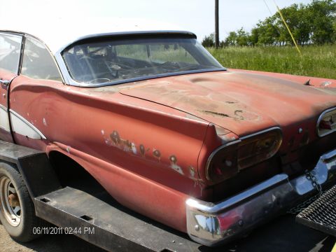 1958 Ford Fairlane - A red 1958 Ford Fairlane with a white roof is seen from the rear quarter, mounted on a trailer and showing signs of wear.