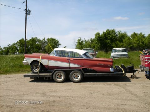1958 Ford Fairlane - A red and white 1958 Ford Fairlane is loaded onto a trailer, with other vehicles visible in the background.