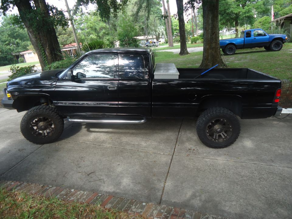 Black pickup truck with chrome side steps and a toolbox in the bed, parked on a concrete driveway
