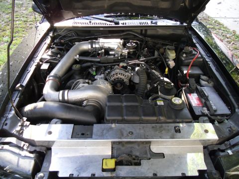 1978 Ford Bronco - Engine bay of a black vehicle with aftermarket modifications, including a large intake pipe.