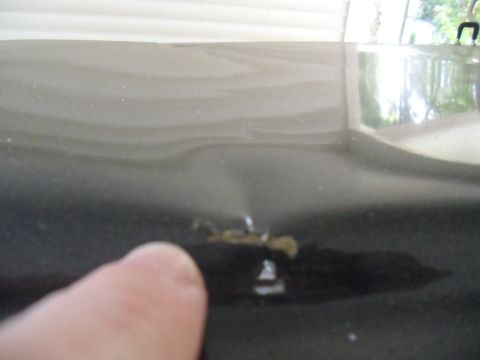 1978 Ford Bronco - A dent is visible on the dark surface of a vehicle's hood, with a finger pointing towards it.