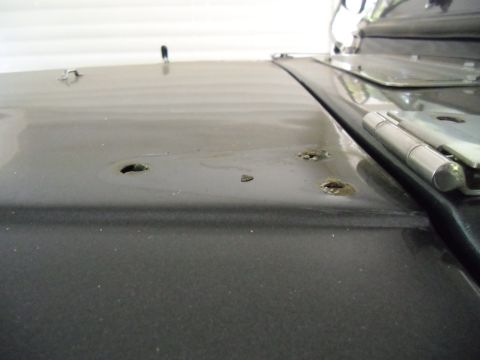 1978 Ford Bronco - Close-up of a car hood's surface, revealing damage and a visible hinge mechanism.