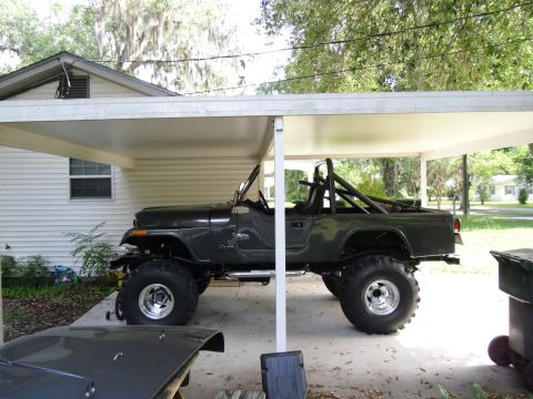 1978 Ford Bronco - A lifted Jeep CJ-7 is parked under a carport, with another vehicle's hood visible in the foreground.