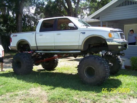 1978 Ford Bronco - A heavily modified pickup truck with oversized tires and a high suspension system is parked on a grassy lawn.