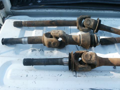 1990 Ford Bronco - Three driveshafts are laid out on a white surface, showing their universal joints and splined ends.