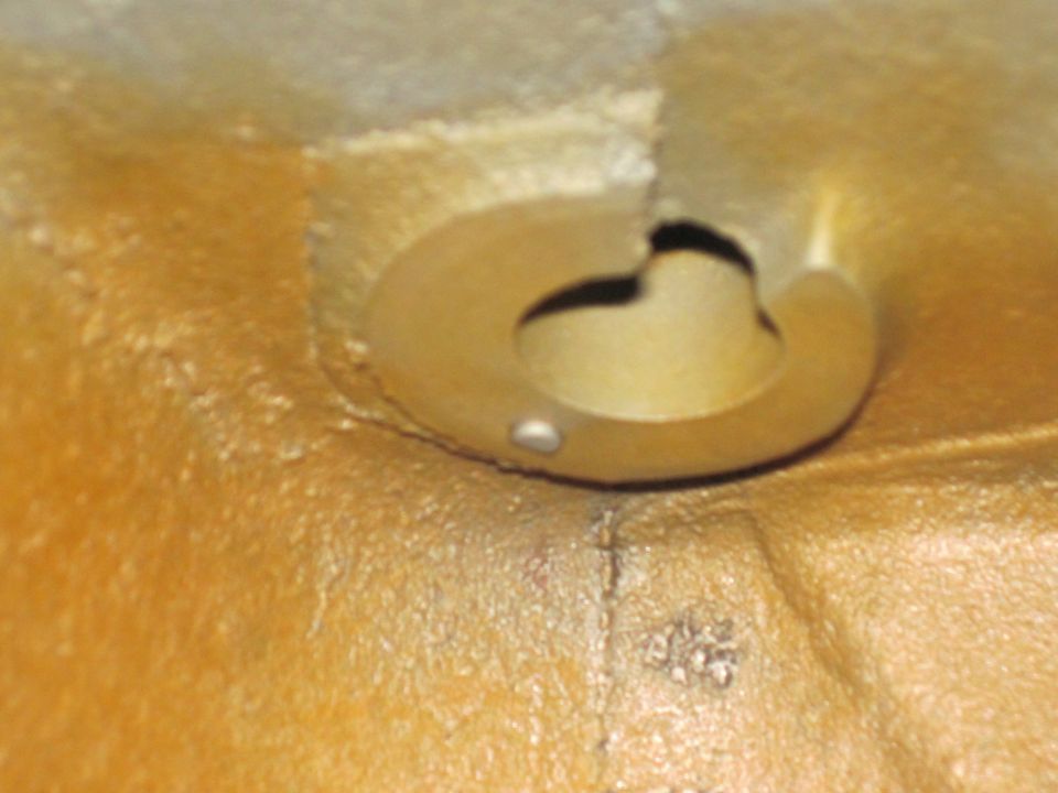 Close-up of a yellow-ish engine part with a circular opening and a small silver pin