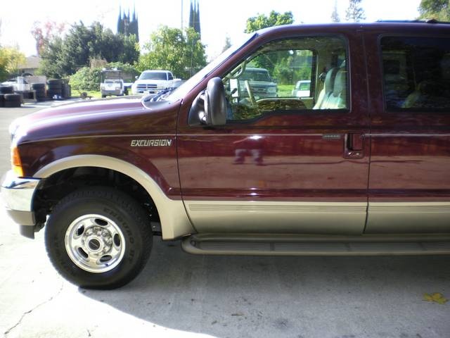 Maroon Ford Excursion SUV, side view. Other vehicles and trees in background