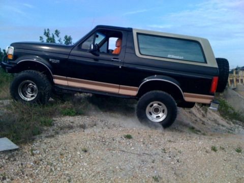 1994 Ford Bronco - Black 1994 Ford Bronco with tan trim driving off-road on a dirt incline.
