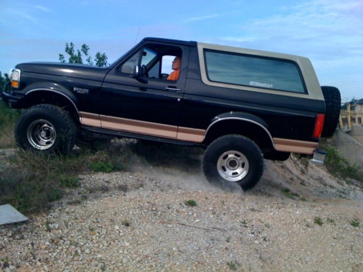1994 Ford Bronco driving up a dirt hill, driver wearing orange shirt