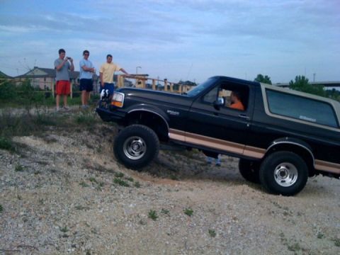 1994 Ford Bronco - A lifted Ford Bronco navigates an off-road trail with onlookers present.