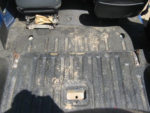 1978 Ford Bronco - The textured floor of a vehicle's interior shows wear and tear, with seat mounting hardware visible.
