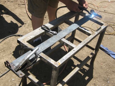 1978 Ford Bronco - A person is welding a metal frame on a workbench in an outdoor setting.