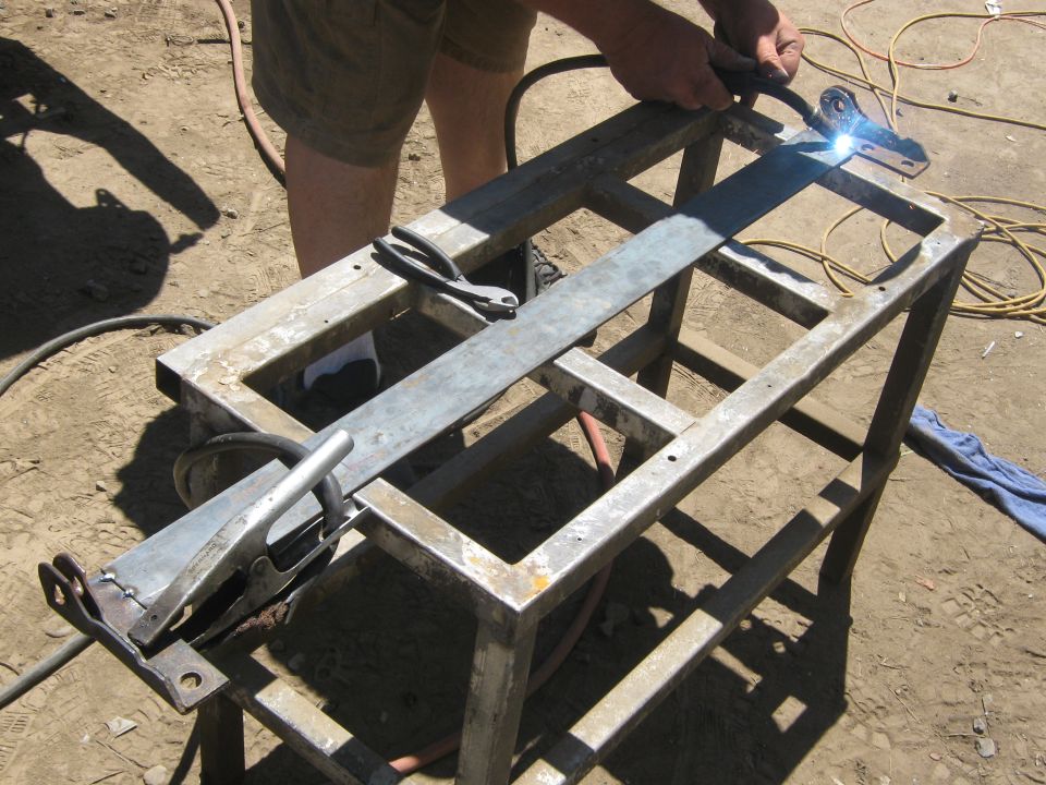 Metal frame being welded outdoors, with tools and welding equipment visible
