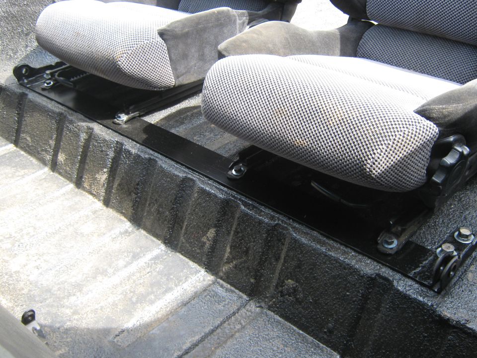 Two fabric bucket seats bolted to black rails over a textured truck bed floor
