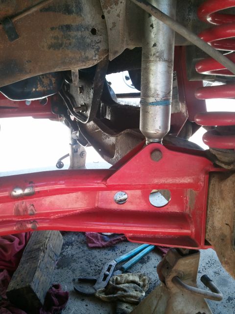 1982 Ford Bronco - Close-up view of vehicle suspension components, including a red suspension arm and shock absorber.