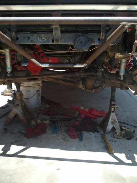 1982 Ford Bronco - The undercarriage of a vehicle is visible, supported by jack stands, with various tools and rags scattered below.