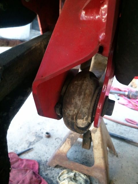 1982 Ford Bronco - A worn suspension bushing is visible, held by a red metal bracket and supported by a jack stand.