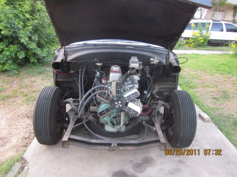 1953 Ford Mainline - The engine bay of a car is exposed with the hood open, revealing the motor and front wheel assembly.