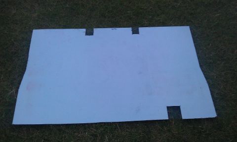 1991 Ford Festiva - A flat sheet-metal or fiberglass panel painted light blue-gray lies face-up on grass, hand-trimmed with notched cutouts along one long edge…