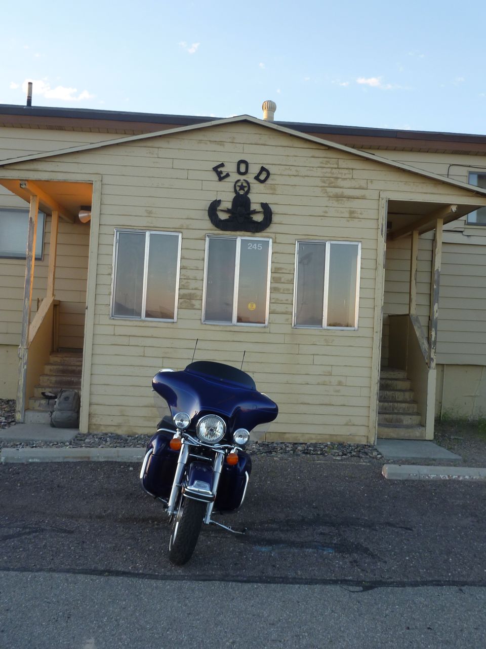 Blue touring motorcycle parked in front of a tan building with an EOD emblem
