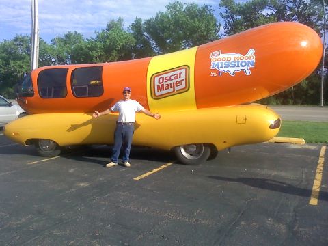 2000 Ford F-250 - A man poses with the iconic Oscar Mayer Wienermobile, a promotional vehicle shaped like a hot dog.