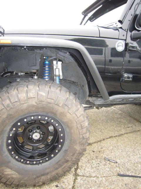 2008 Jeep Wrangler - Front driver-side view of a black Jeep Wrangler JK showing a blue-spring coilover with remote-reservoir shock in the open wheel well, a bla…