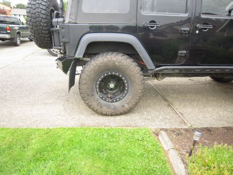 2008 Jeep Wrangler - Passenger-side rear quarter of a lifted black four-door Jeep Wrangler on a concrete driveway, showing a mud-terrain tire on a black beadloc…