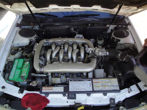 2003 Ford Taurus - The engine bay of a white car is shown with a V8 engine, Interstate battery, and various labels visible under the hood.