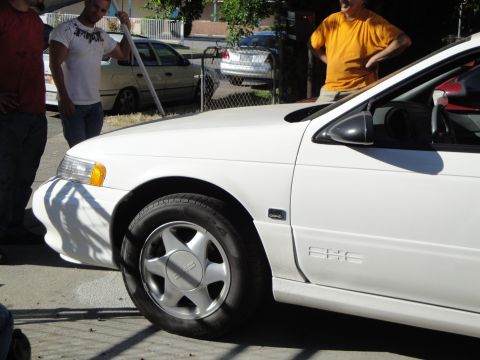 2003 Ford Taurus - A white sedan is parked outside with several people around it. A second car is visible in the background.