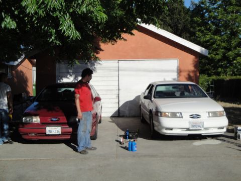 2003 Ford Taurus - A white 2003 Ford Taurus is parked in front of a garage, with a red car to its left.