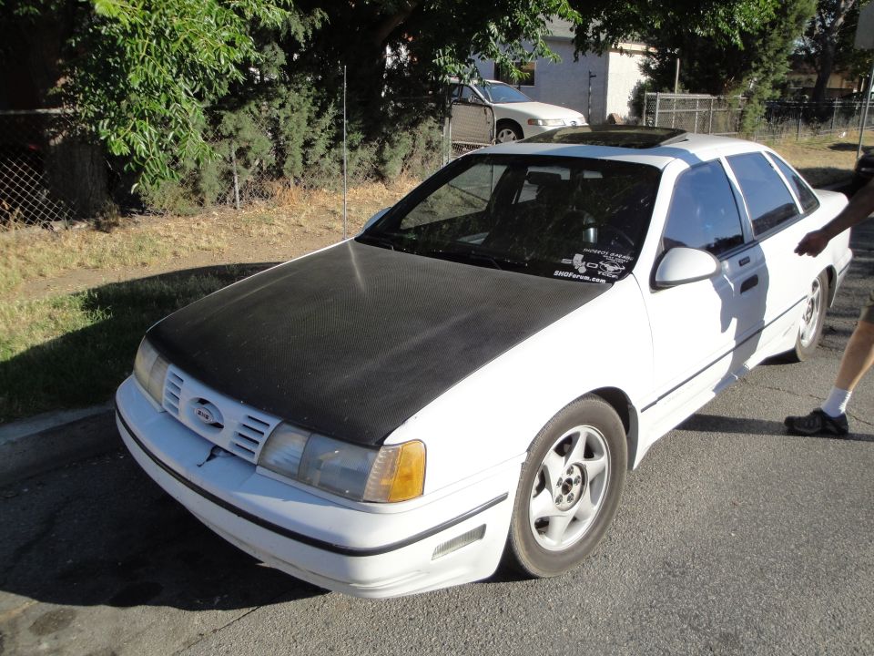 White sedan with a black hood, sunroof, and aftermarket wheels parked on a street