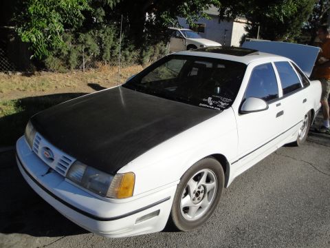 2003 Ford Taurus - A white sedan with a black hood and a sunroof is parked on a street, with another vehicle visible in the background.