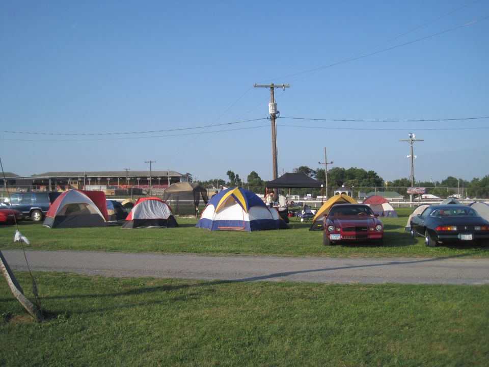 Several tents set up on a grassy field with a few cars parked nearby under a clear blue sky