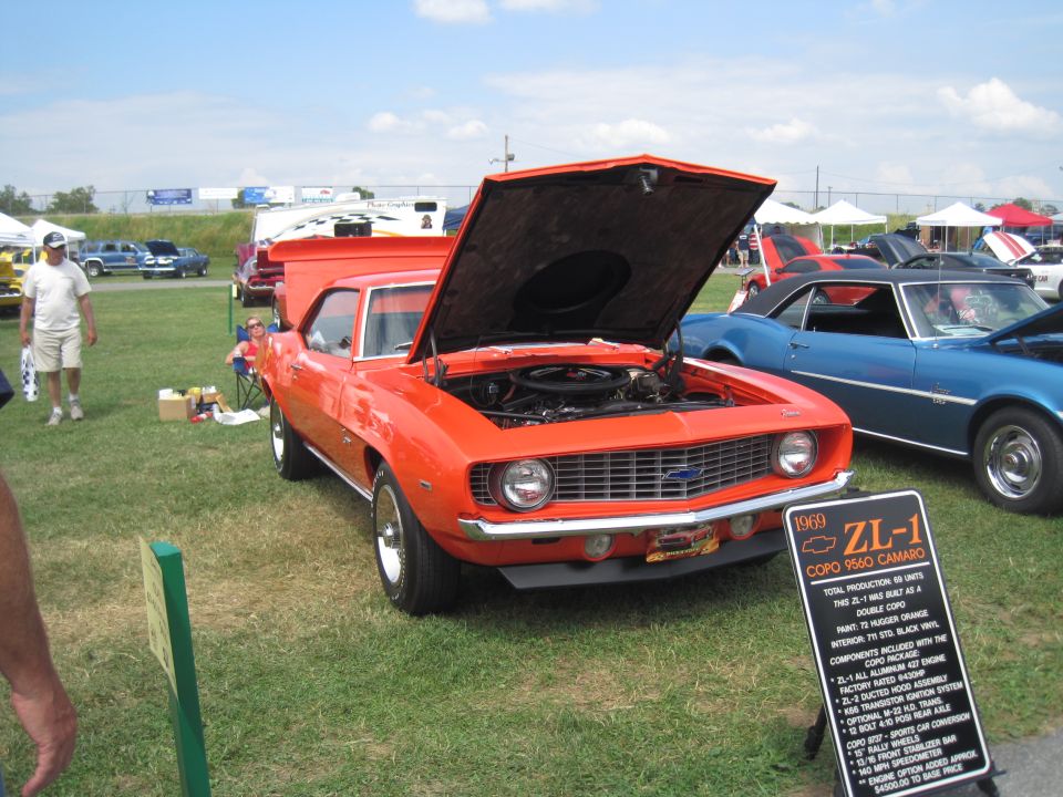 Orange 1969 Camaro ZL-1 with hood open, parked next to a blue Camaro. Sign in front details the car