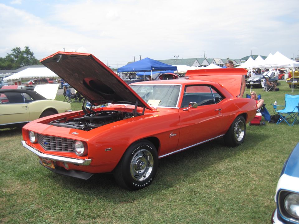 Orange 1969 Chevrolet Camaro coupe with hood and trunk open, parked on grass at an outdoor event