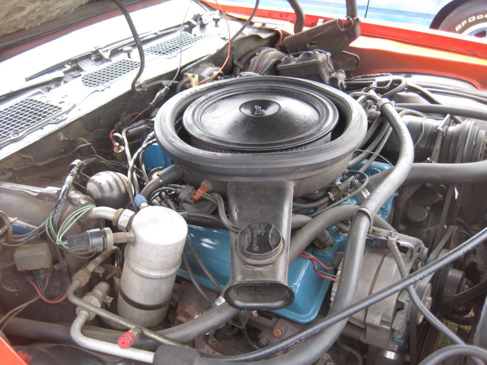 Close-up of a car engine with a black air filter housing over a blue engine block. Wires and hoses are visible