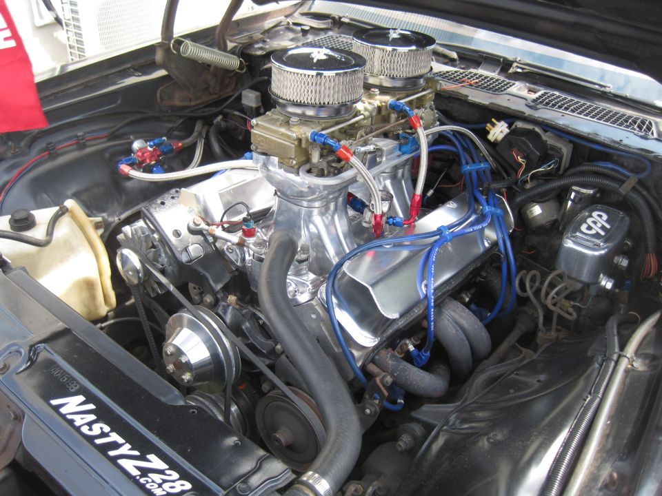 Engine bay with dual carburetors, chrome valve covers, and "NASTY Z28 .COM" sticker on the radiator support