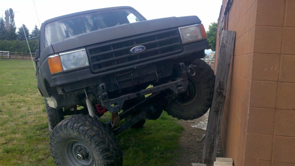 1987 Ford Bronco with large tires leaning against a brick wall